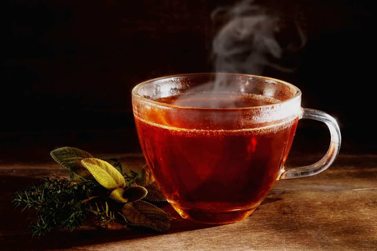 a hot cup of orange tea sitting next to green leaves on a brown table