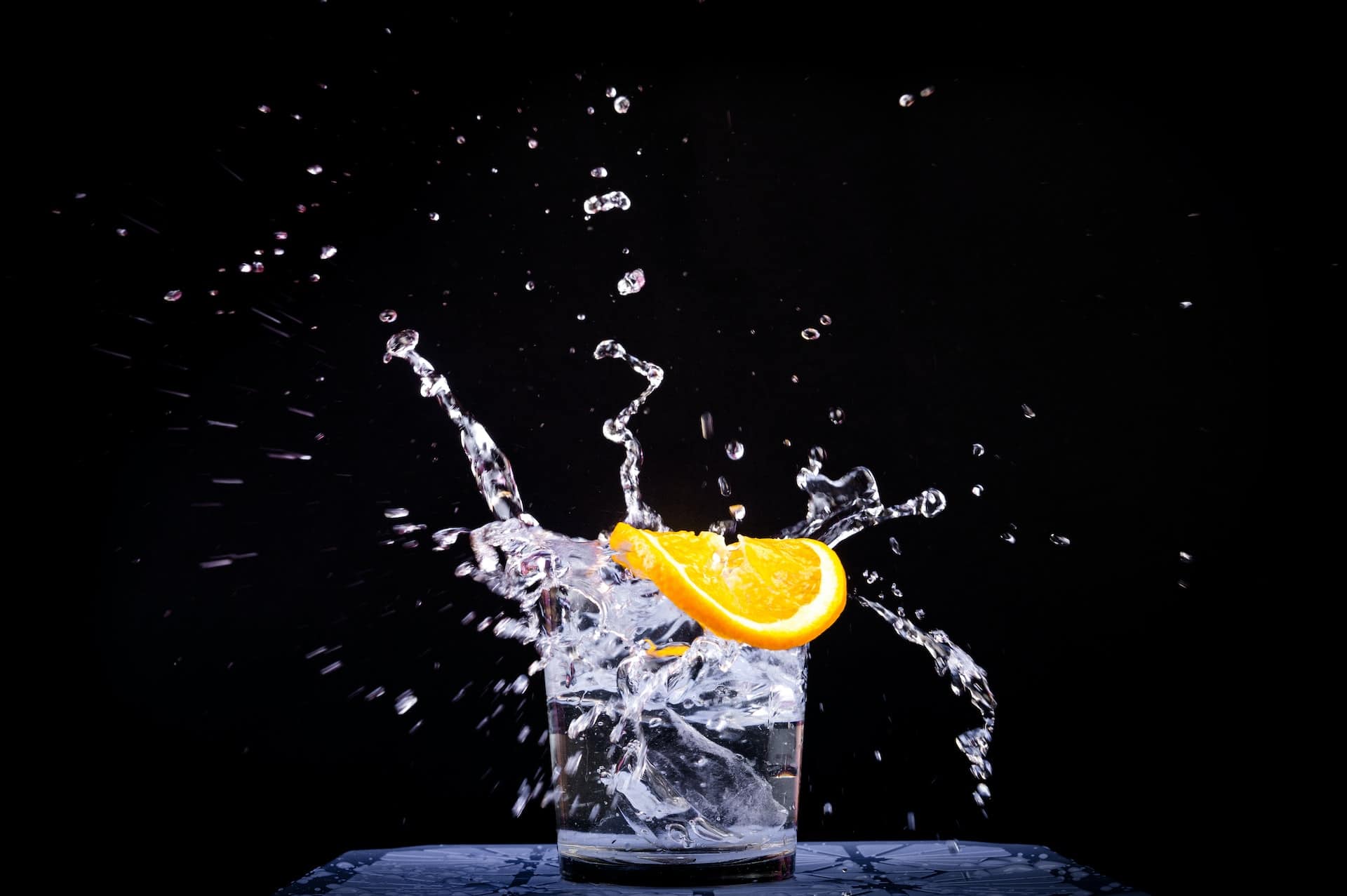 A glass of water and a slice of orange being splashed