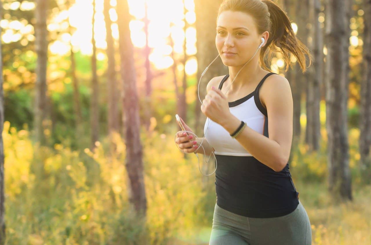 woman with a ponytail jogging through a forested trail and listening to music