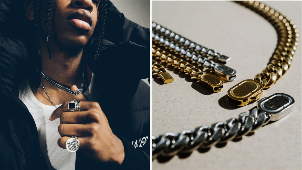 Man wearing a white t-shirt and black coat. His hand is holding out a thick silver cuban link chain that he's wearing around his neck