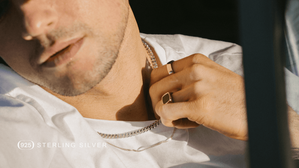 Close up of man sat in car looking out the window. Hw's wearing a plain white t-shirt and Sterling Silver accessories