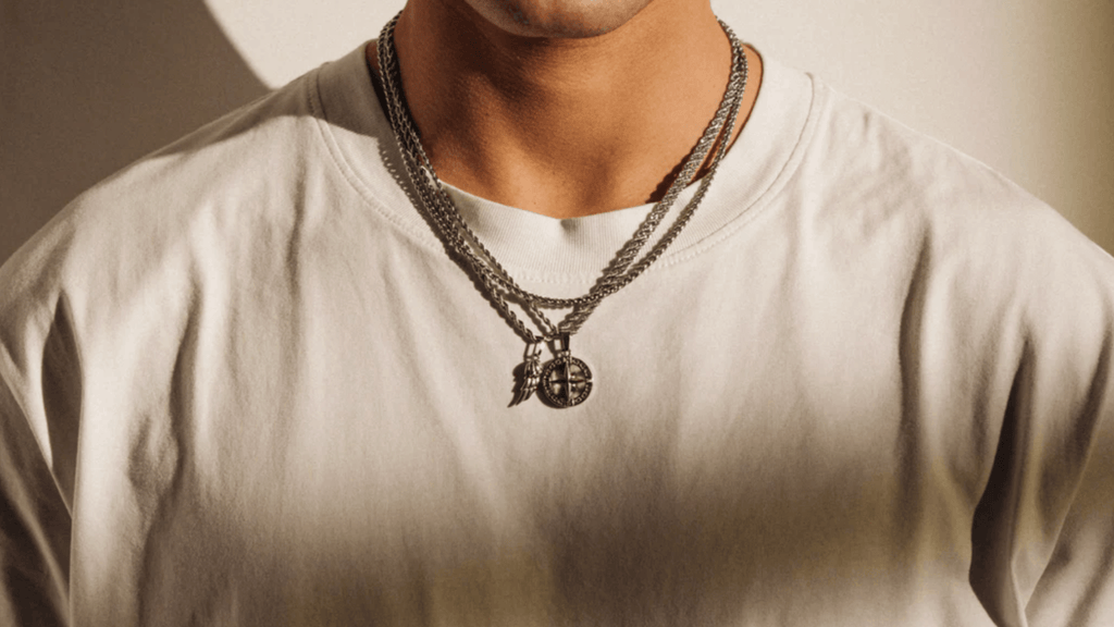 Man wearing a plain white t-shirt and layering silver necklaces, chains and pendants