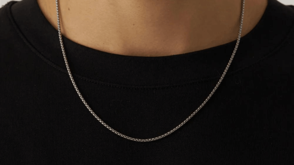 Close up of a man's chest wearing a plain black t-shirt and a silver Box Chain