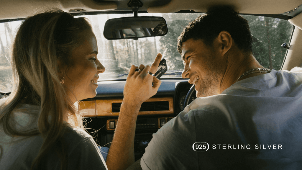 Man and woman sat laughing in inside of a classic car to highlight the authentic and romantic nature of the classic sterling silver jewellery the man is wearing