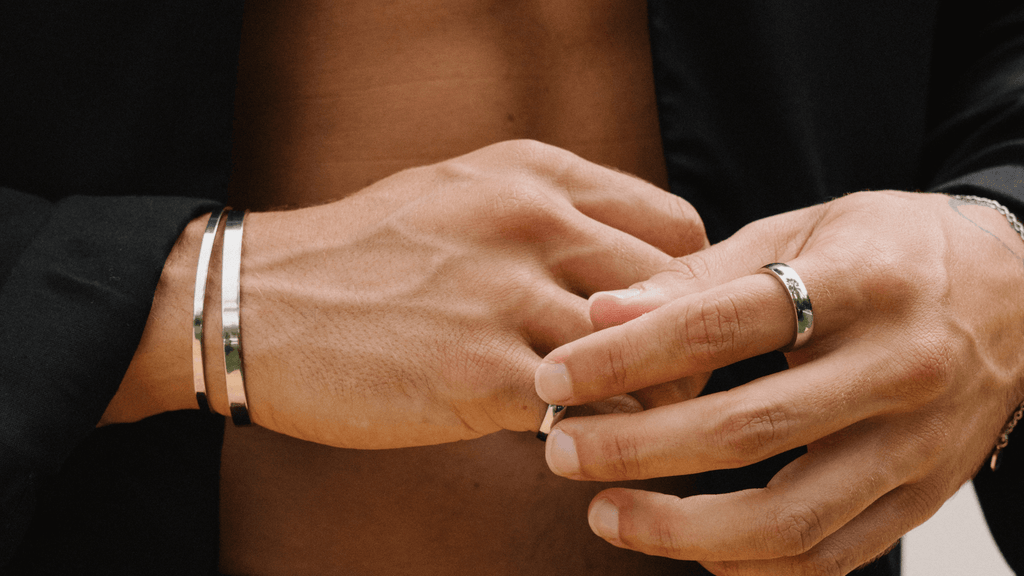 Man's hands styling silver jewellery including simple signet rings and sleek cut bracelets