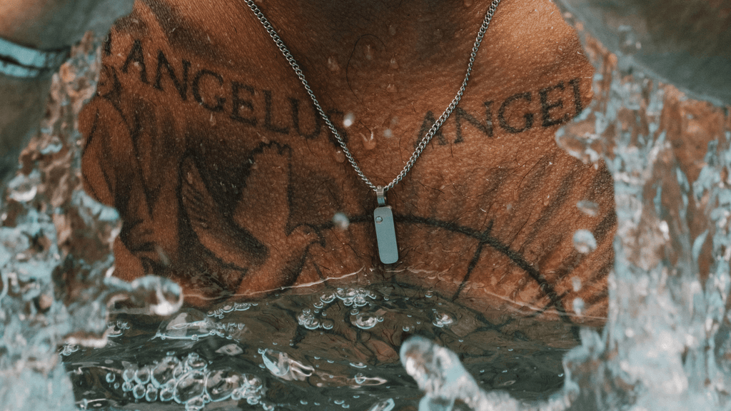 Man submerged in pool water with it splashing and dripping off his silver totem pendant necklace