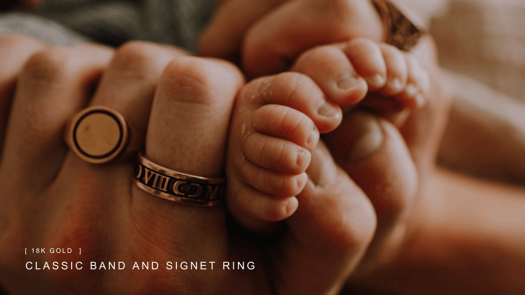Father's hands wrapped around his new born babies feet. His fingers are adorned with gold signet rings