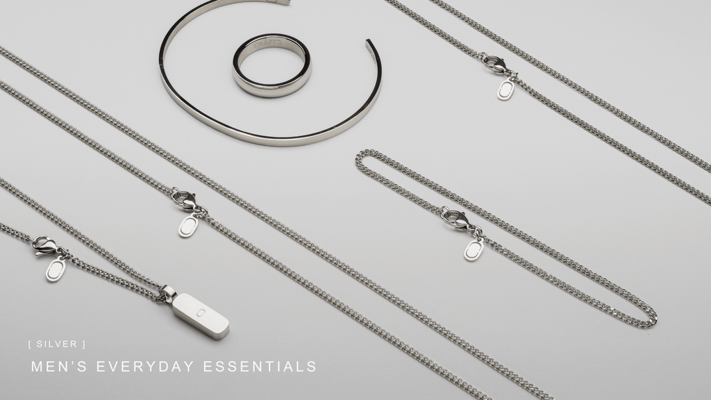 A Collection of essential men's jewellery laid on a grey table including box chains and box chain bracelets