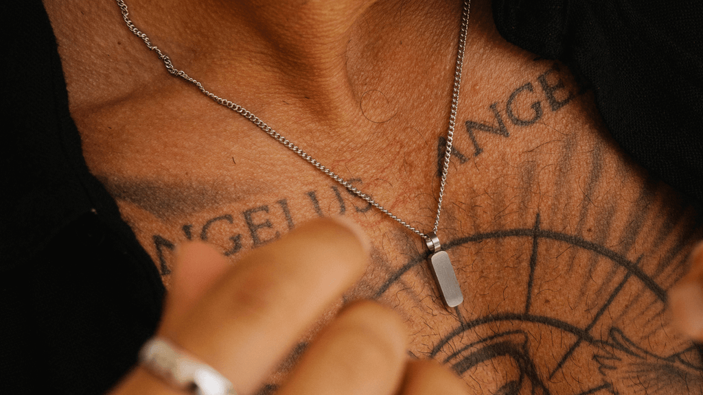 Man's tattoo'd chest with a single silver totem pendant necklace dropping down