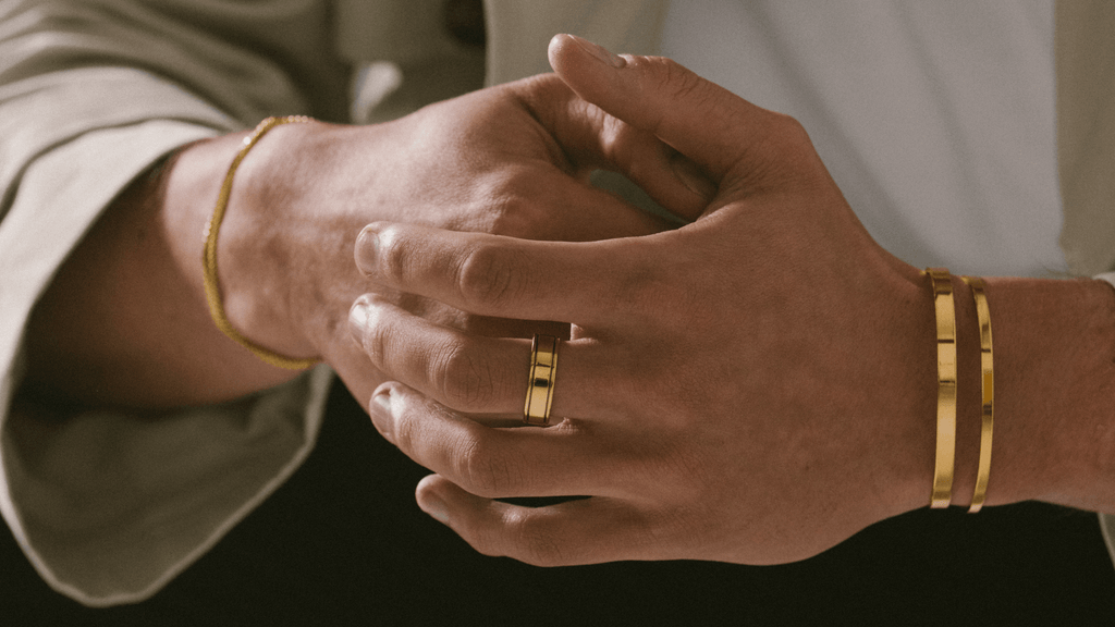 Man's hands styling different types of men's gold jewellery including signet rings, bracelets and cuffs