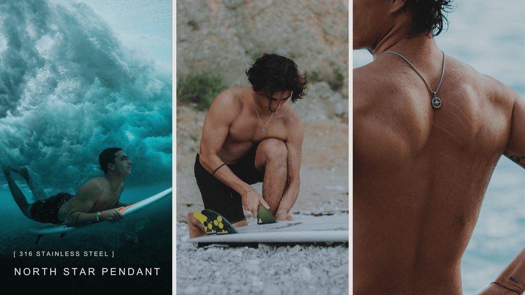 Young topless man at the beach working on and also riding his surfboard amongst the crashing waves. He's wearing a silver stainless steel North Star pendant to symbolise his passion for adventure