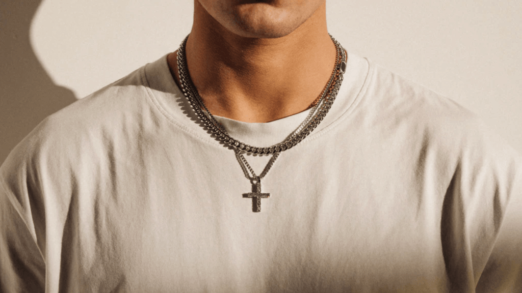 Man with a plain white t-shirt layering a silver necklace and cuban link chain