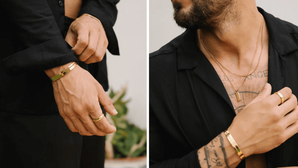Man wearing a plain black shirt and styling simple gold jewelry including signet rings and plain cuff bracelets