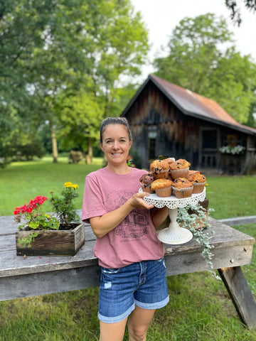 Woman holding blueberry muffins in front of homestead 1800 farmhouse blueberry farm