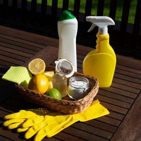 A basket of natural cleaning supplies on a wooden deck with a green lawn and trees in the background