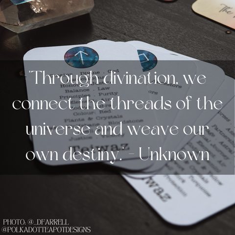 A photo of a card with a quote about divination written in white text on a black background, surrounded by other cards with blue circles and astrological symbols on them. The quote says “Through divination, we connect the threads of the universe and weave our own destiny. - Unknown”.