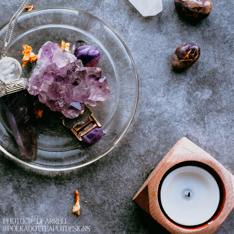 A photo of a collection of crystals and a candle on a grey surface. The crystals are arranged on a round, silver tray.