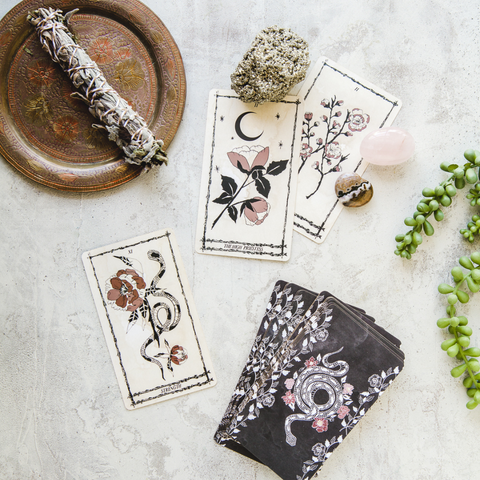 A flat lay photo of tarot cards, a smudge stick, and other objects on a white background.