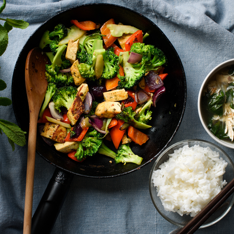 A photo realistic image of a skillet of stir fry on a blue-grey tablecloth