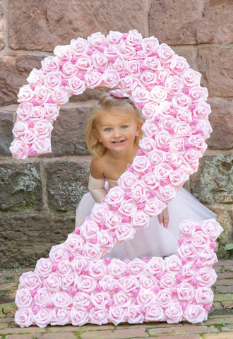 cute little girl peeks around wooden number two covered with pink roses