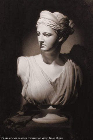 Photo of Cast Drawing of Plaster Cast of Diana of Versailles bust - female goddess with drapery and crown and up-do - on a table with a cloth over it and rolled into folds beside the statue with a black background
