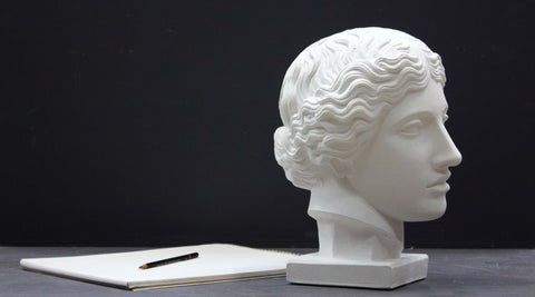 Photo of plaster cast of an Amazon Head with a sketchpad and pencil to the left on a black background