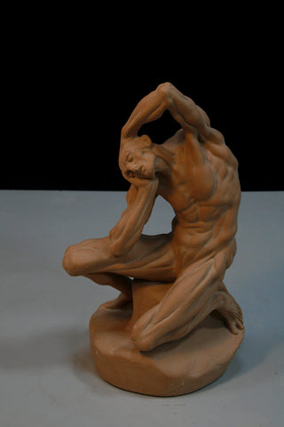 photo of plaster cast of terracotta-colored anatomical man kneeling and holding head on gray and black background