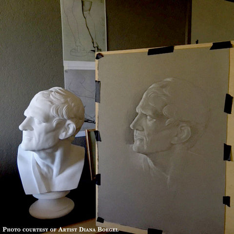 Photo of Cast Drawing of Plaster Cast of Bust of a Man - head turned to his right and a sash on his right shoulder - taped to an easel with the actual cast to its left and drawings on the dark background behind them