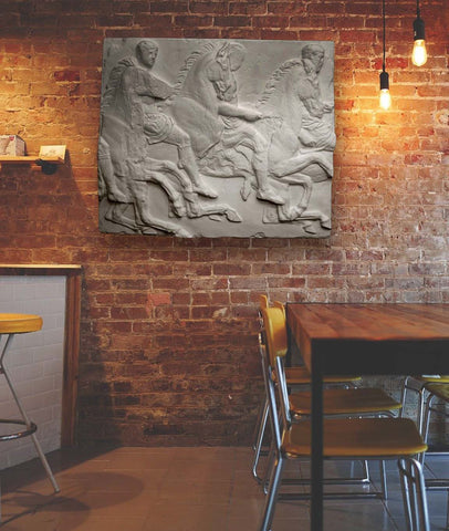 Photo of plaster cast sculpture of men on horses Parthenon Frieze on brick wall with table and chairs on right and bar on left, cropped