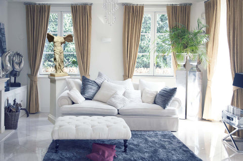 photo of white-walled living room with white, blue, and gold furnishings with two plants in urns in a corner and reduction Victory of Samothrace plaster cast sculpture to the left