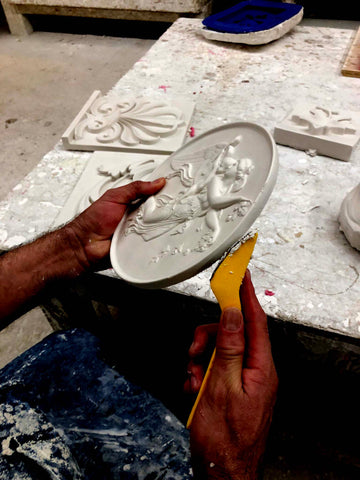 closeup of someone's hands using a tool on a newly-made plaster cast of a flying female figure