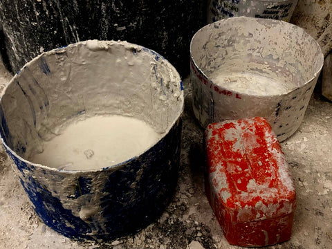 three buckets - blue, red, and clear - with plaster in them and on and around them