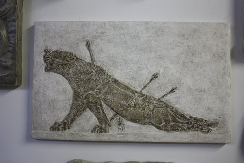 photo of plaster cast sculpture of a wounded lioness with arrows in her back in a two-toned finish on a white wall