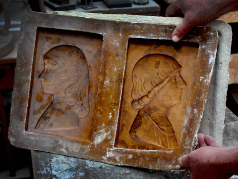 Photo of a hand holding a brown silicon mold of two sculptural relief portraits