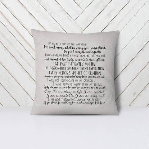 Photo of off-white pillow with rows of lyrics in black leaning against a white wall and on a white bed