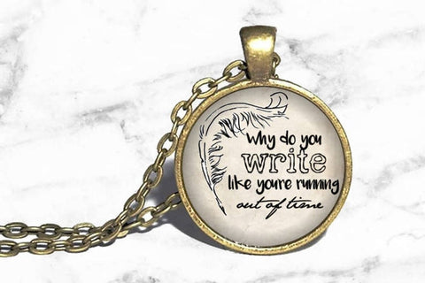 Photo of gold round necklace with lyrics and quill in black
