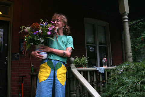 owner of part-time poodle wearing linen pants with lemon pockets holding a vase of flowers