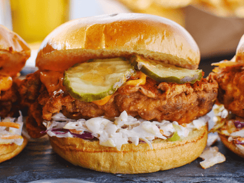 Close-up of a spicy fried chicken sandwich with pepper jelly sauce, pickles, and coleslaw