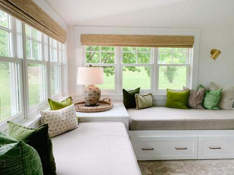 Two built in day beds with storage drawers, under windows with custom grey mattress covers, decorated with a selection of green and neutral throw pillows. 