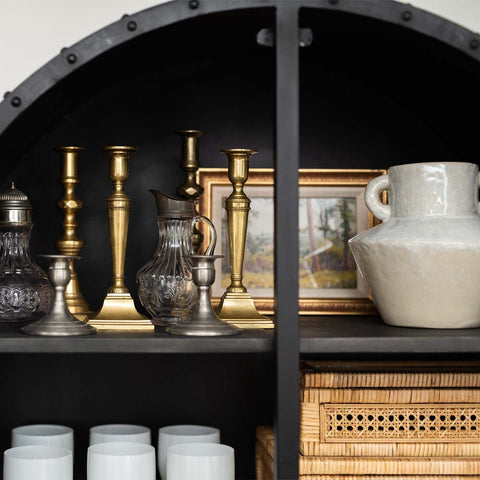Black cabinet with collection of brass and pewter candlesticks