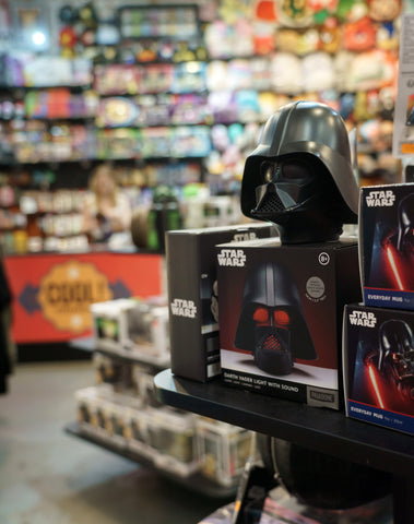 A Darth Vader replica helmet sits on a store shelf full of Star Wars merch.