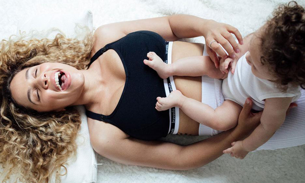 A woman wearing a black bravado nursing bra holds a baby on her stomach