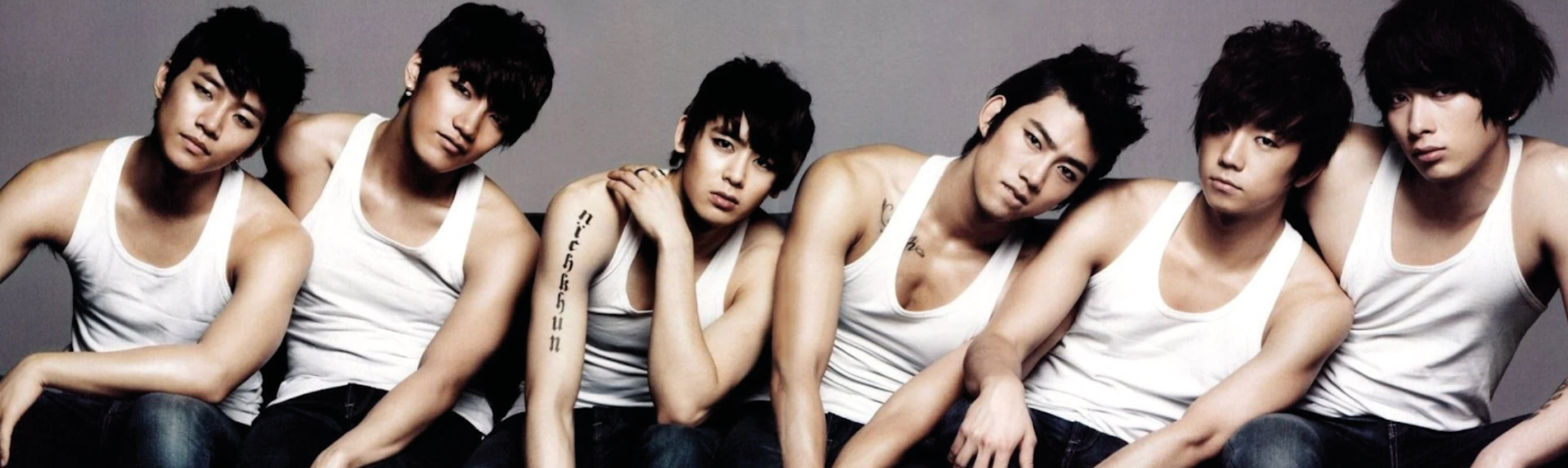 2pm members taecyeon jun.k chansung junho wooyoung nichkhun sitting in a row next to each other wearing white tops bare arms