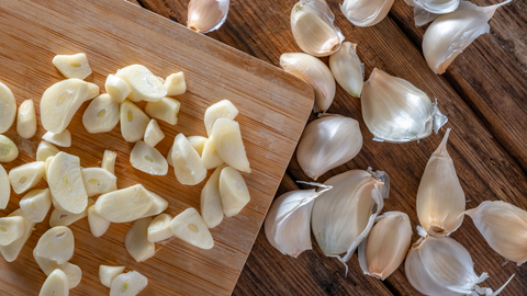 Chopped Garlic On Cutting Board Next To Garlic Cloves On Kitchen Counter