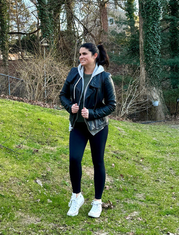 Woman wearing black leggings, a grey hoodie, and a black leather coat posing the soccer mom look number 1