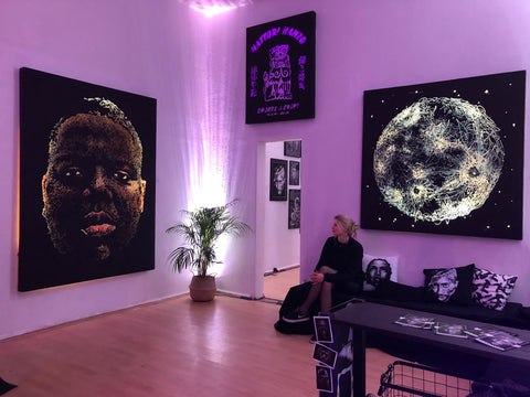 The artist Marilena Hamm alias Scribblezone sitting in her gallery in Mannheim's Jungbusch, her light paintings and illuminated portraits can be seen on the walls.
