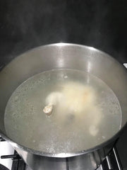 Boiling chicken in large pot for Hainanese chicken rice dish.