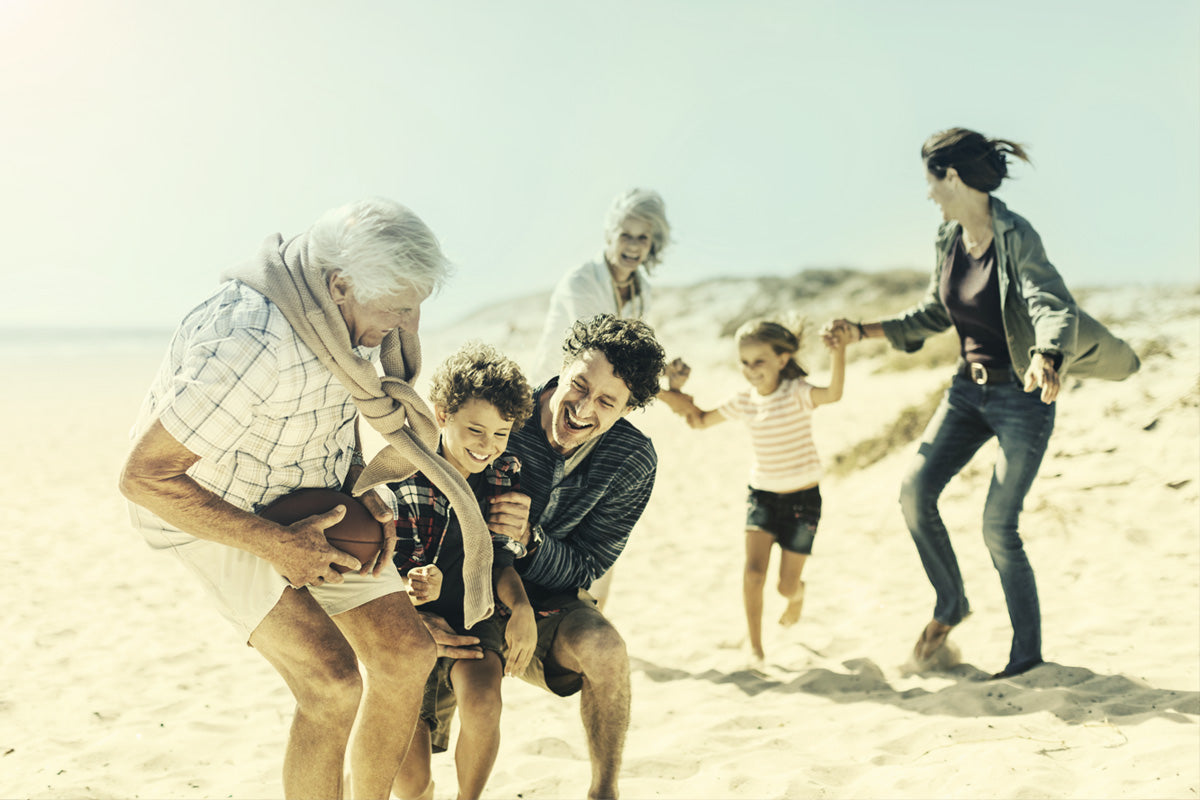 A photo of a family, grand parents, parents and their two kids playing on the beach sand on a sunny day.