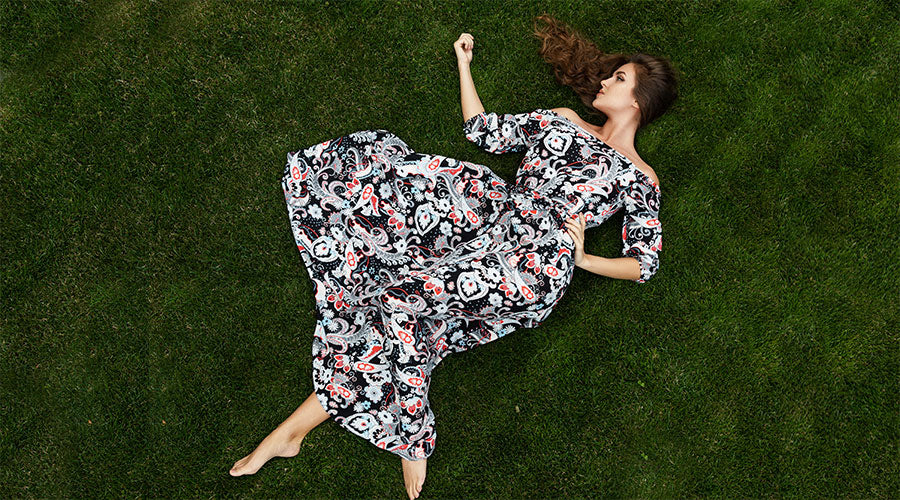 Portrait of gorgeous woman wearing beautiful maxi dress lying on a lawn with the green grass