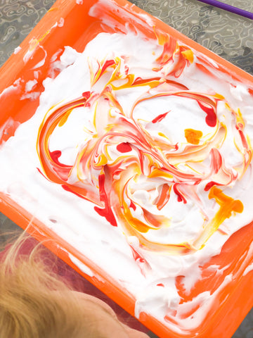 activity tray filled with shaving cream and drizzled with red, orange, and yellow paint to create marbled painting for toddlers and preschoolers